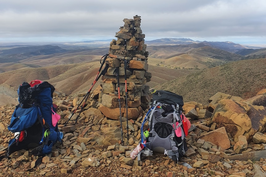 Two hiking back packs on top of a mountain, next to a large rock cairn