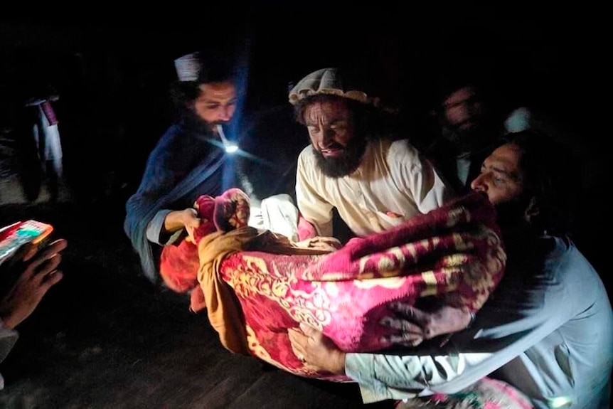 A man in Afghanistan carries a wounded person in their arms, bundled in a blanket, after the earthquake which struck the country