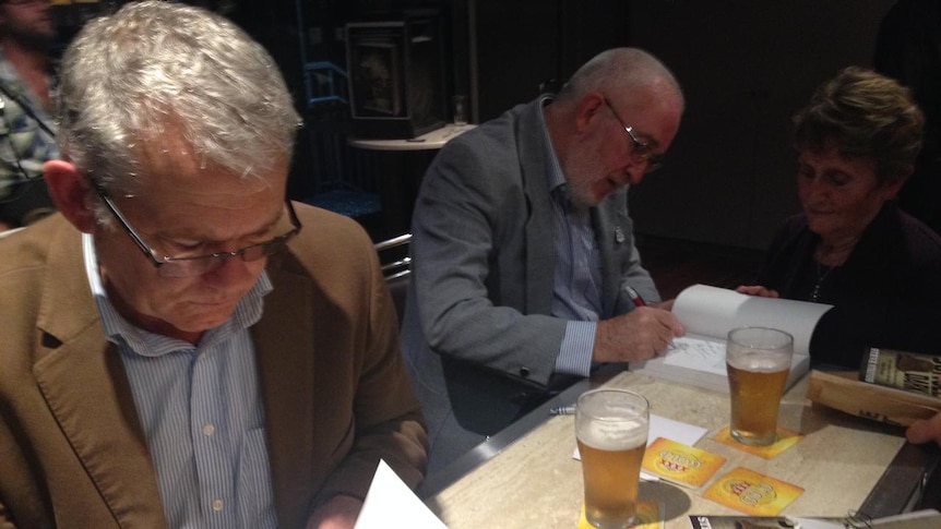 Two men sitting at a table signing books