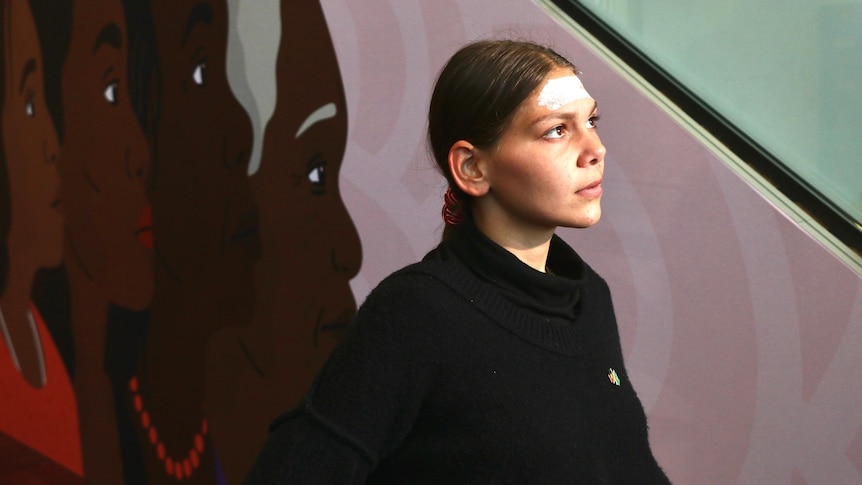 A young woman with traditional paint on her forehead looks into the distance.