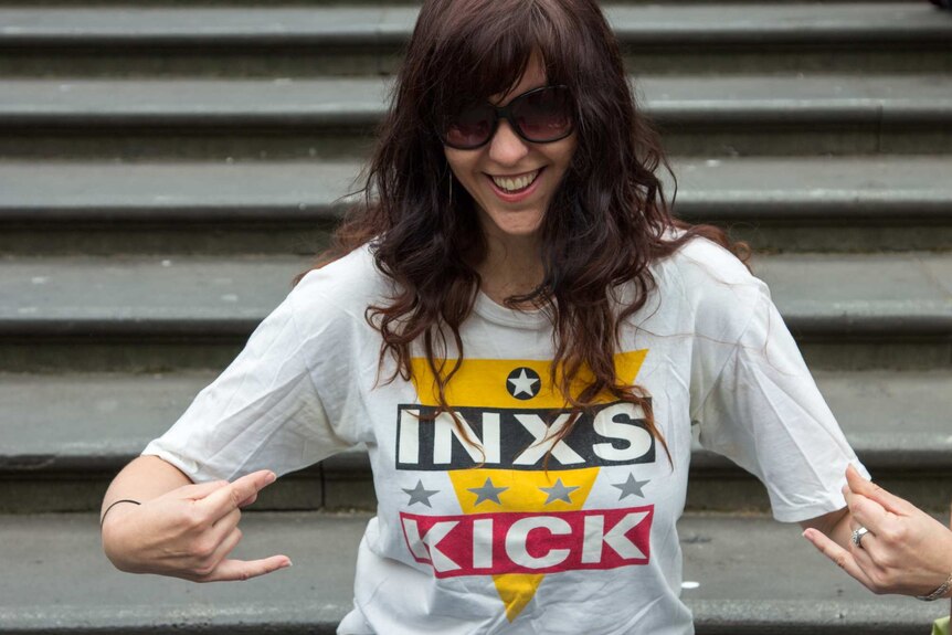 A woman sitting on stairs points at her INXS t-shirt.