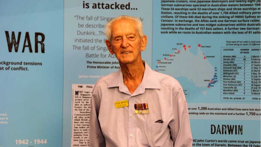 WWII veteran Peter Hackett in front of a museum exhibit board about Australia under attack.