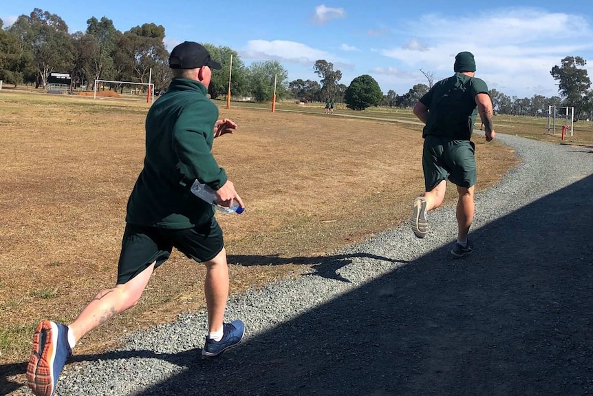 Two prisoners in green shorts and top run along gravel path