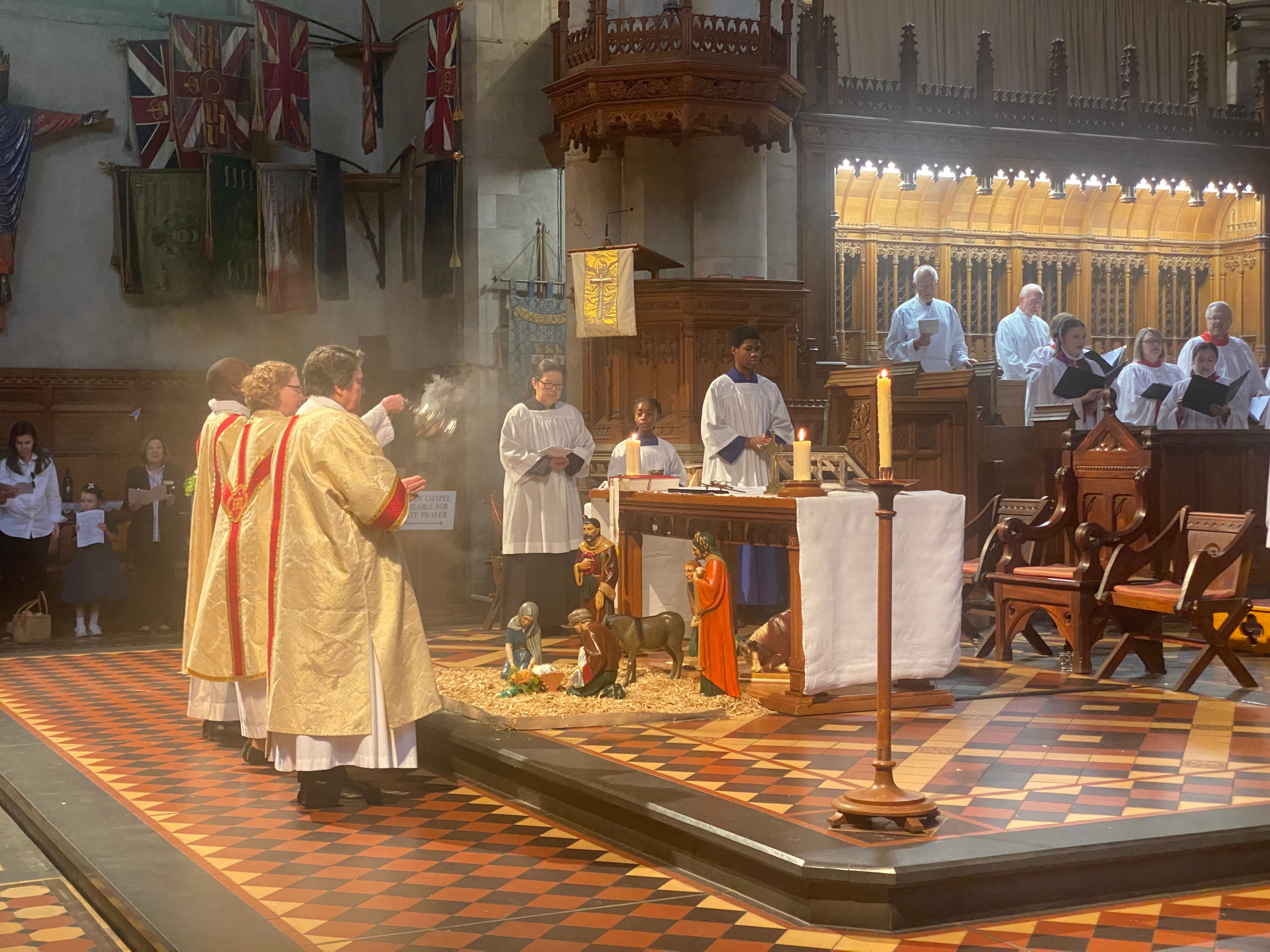Miniature statues are laid out in the middle of a checkered-tiled stage and surrounded by churchgoers