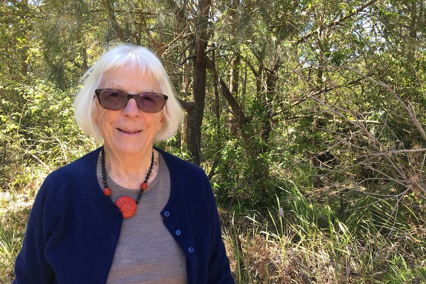 An elderly woman in a blue cardigan smiles at the camera