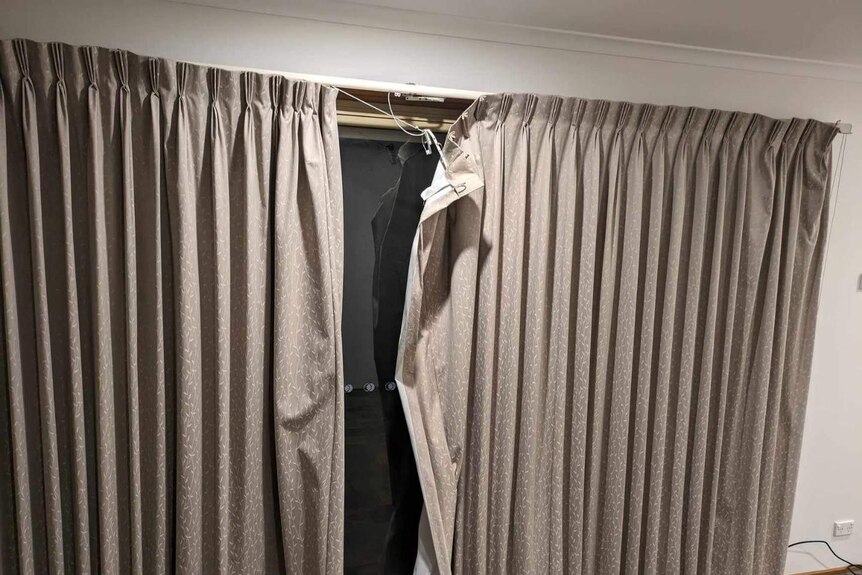 Damage to the rod of beige curtains in a home.
