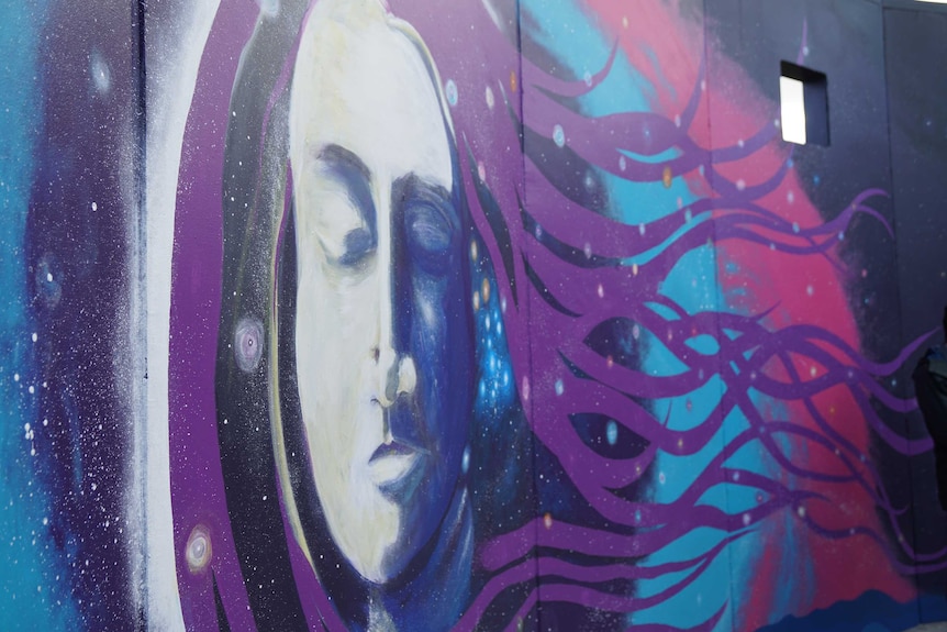 A woman's face with her eyes closed and flowing hair painted on a wall.