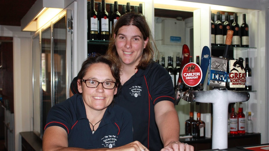 Two women stand behind a pub bar