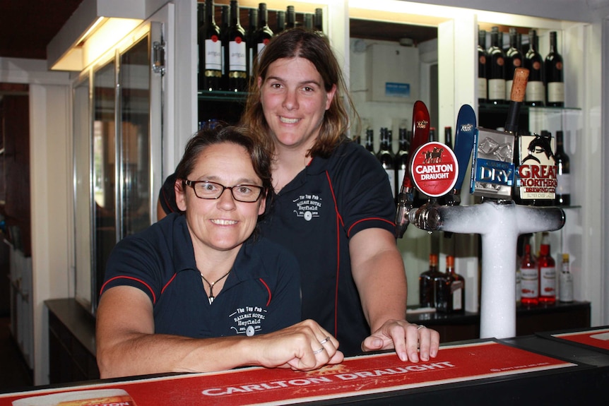 Two women stand behind a pub bar