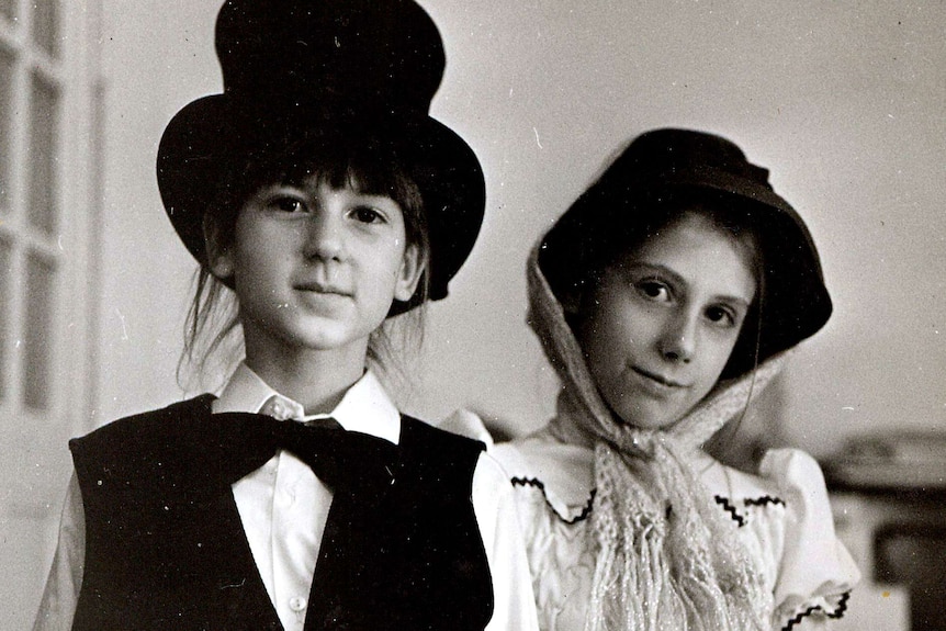 Black and white photo of Kathrin as a girl, dressed up in a white dress, next to a friend dressed up in a suit and tophat