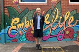 Teenager in school uniform standing in front of a painted mural.