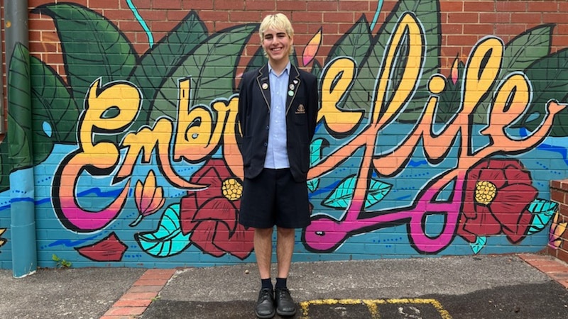 Teenager in school uniform standing in front of a painted mural.