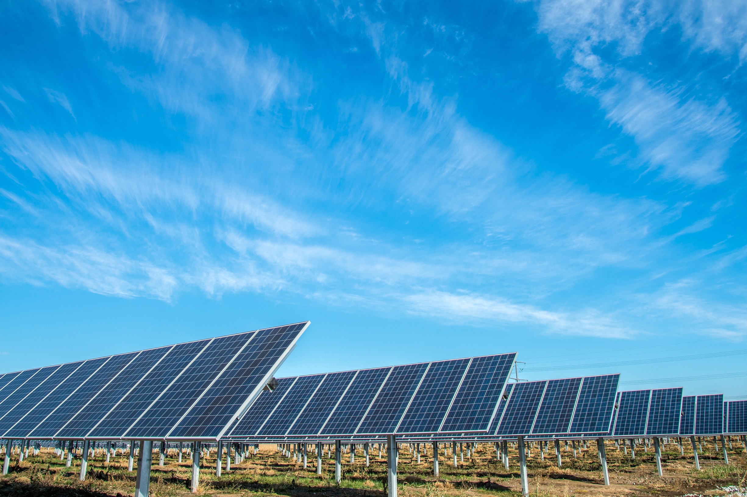 Solar panels line up under a bright blue sky.