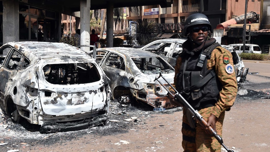 A Burkina Faso gendarme stands guard next to burnt cars outside Splendid Hotel.