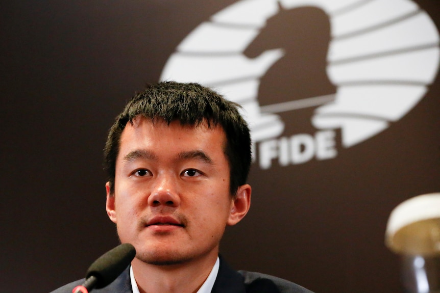 Chess world champion Ding Liren sits in front of the logo of the logo for chess's world governing body.