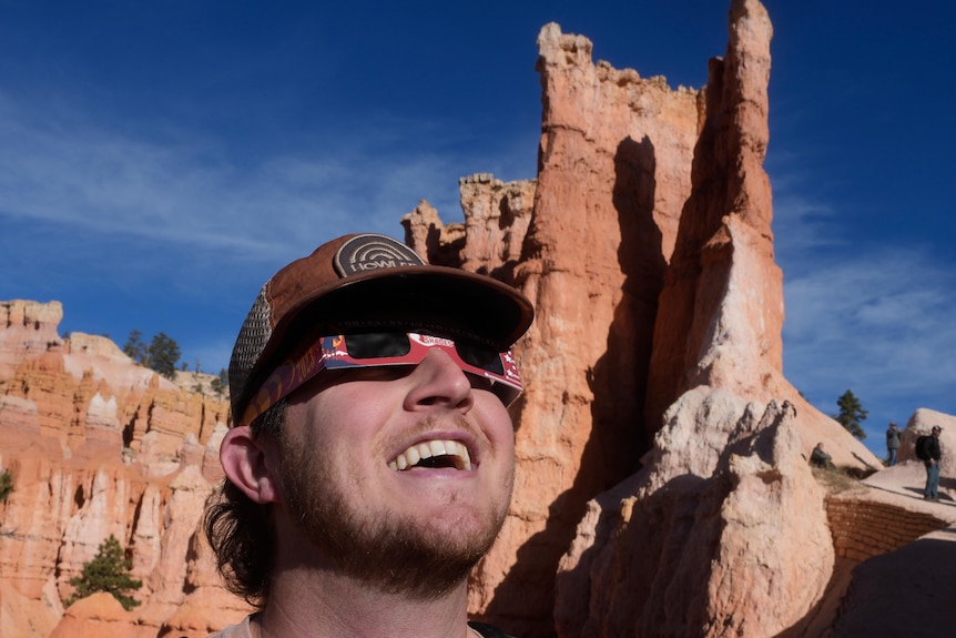 A man wearing eclipse glasses looking up at the sky with Utah rock formations in the background