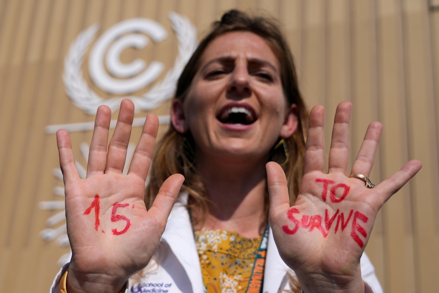 A woman in a white labcoat holds up the palms of her hands to the camera. '1.5 to survive' is written on her palms