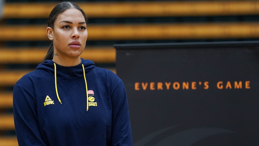Basketballer Liz Cambage stands looking serious, next to a sign saying "Everybody's Game".