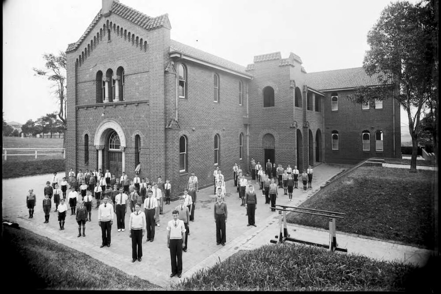 A black and white vintage photograph of students standing in formation outside a church. 