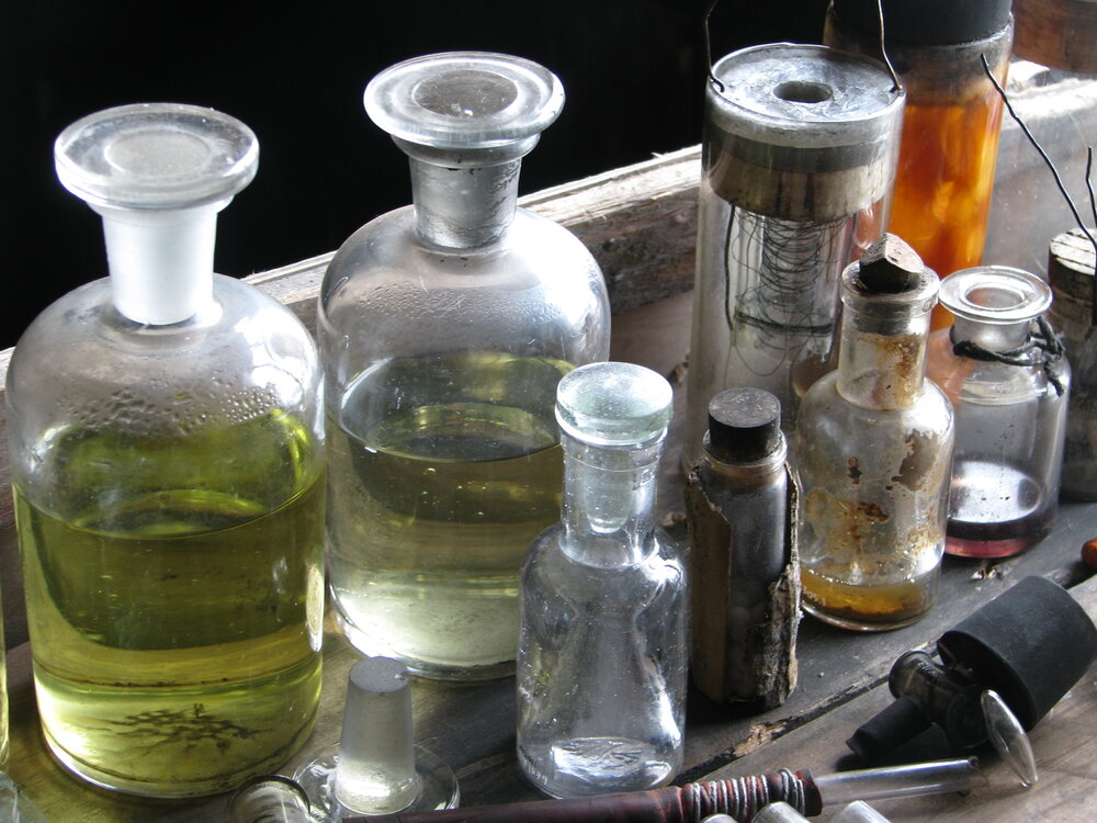 An array of old bottles with green liquid and other scientific equipment on a table. 