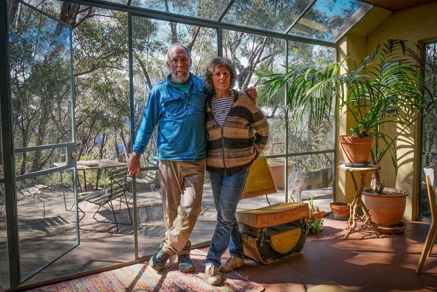 Rolley and Robin Clarke standing in their home, surrounded by bushland.