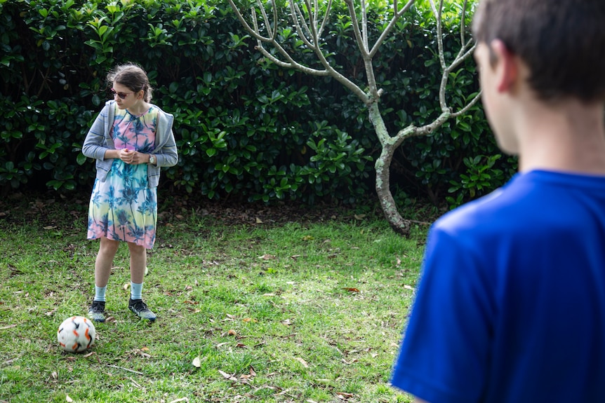 a young girl standing on the grass with a round ball as a young boy watches on 