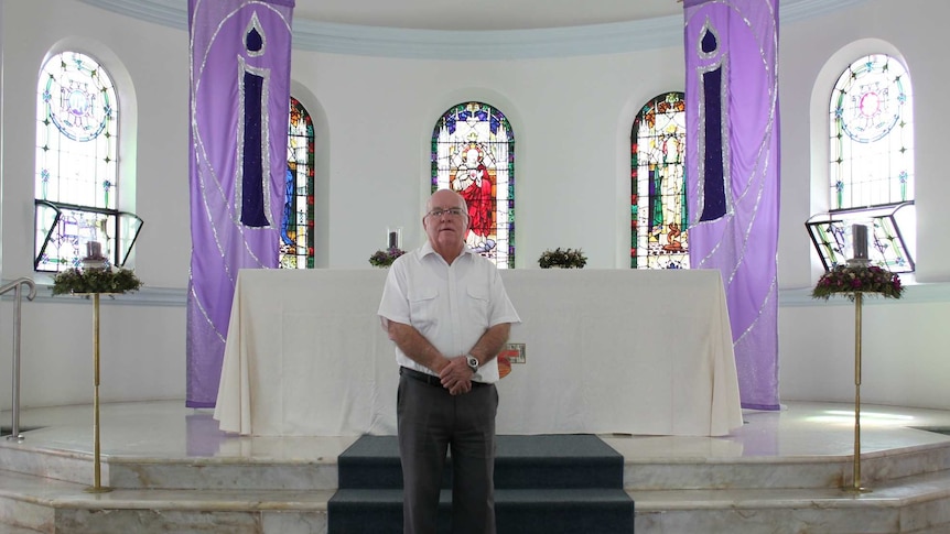 An older priest stands in front of the altar in Holy Rosary Church.