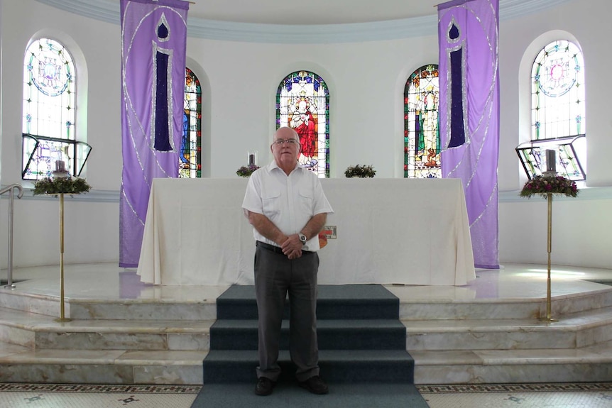 An older priest stands in front of the altar in Holy Rosary Church.