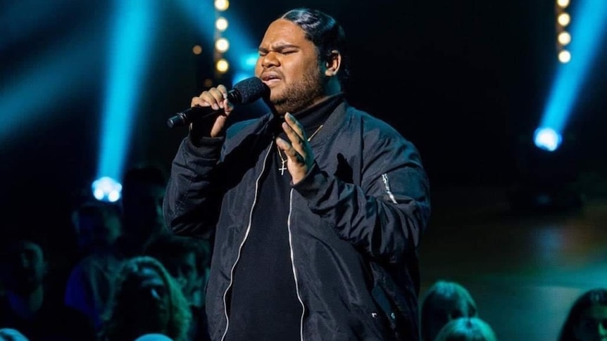 A man dressed in black sings on a stage in a TV studio.