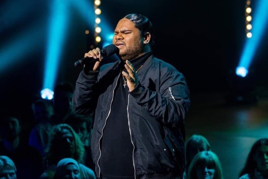 A man dressed in black sings on a stage in a TV studio.