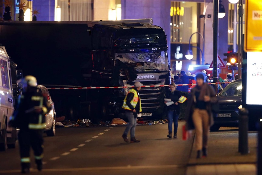 The truck with a smashed windscreen lays still in the road.