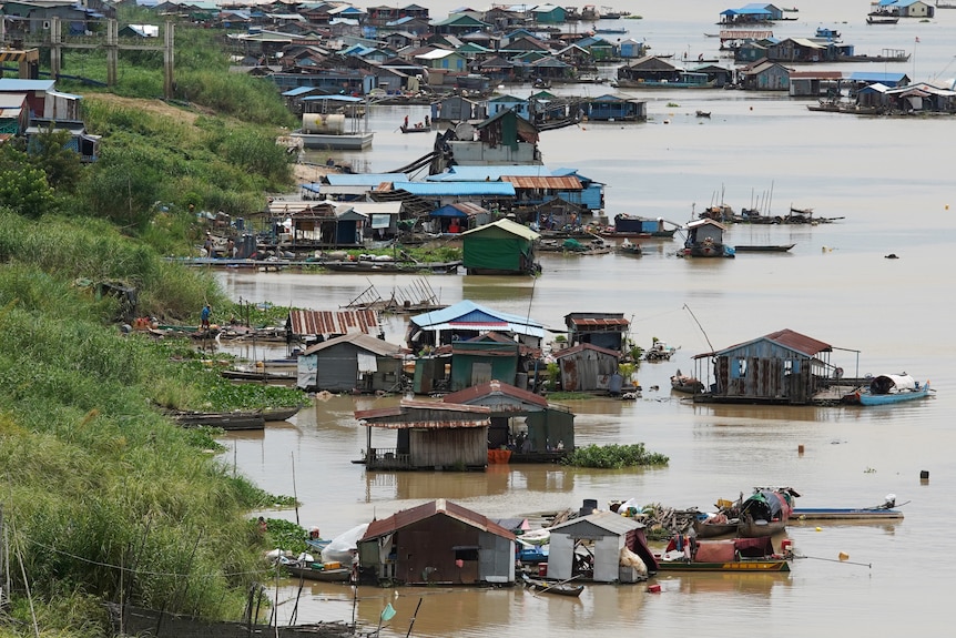 An aerial view shows several houses floating on a brown river next to a green grassy bank