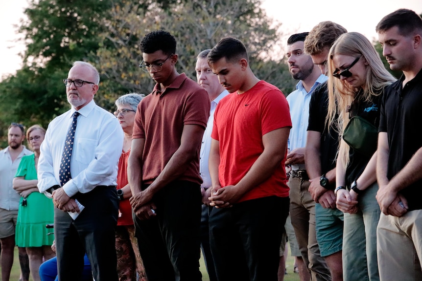 A group of people bow their heads and hold their hands together during a minute's silence