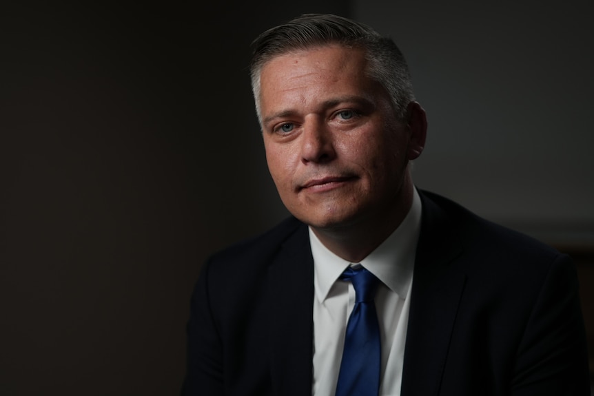 A man with shot grey hair in a black suit nd blue tie