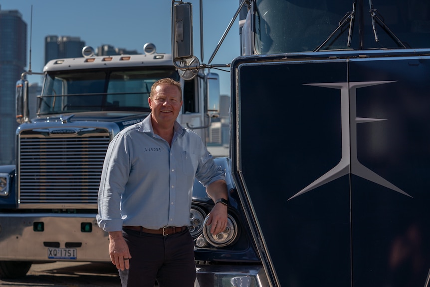 Man leaning on truck with another large prime mover behind