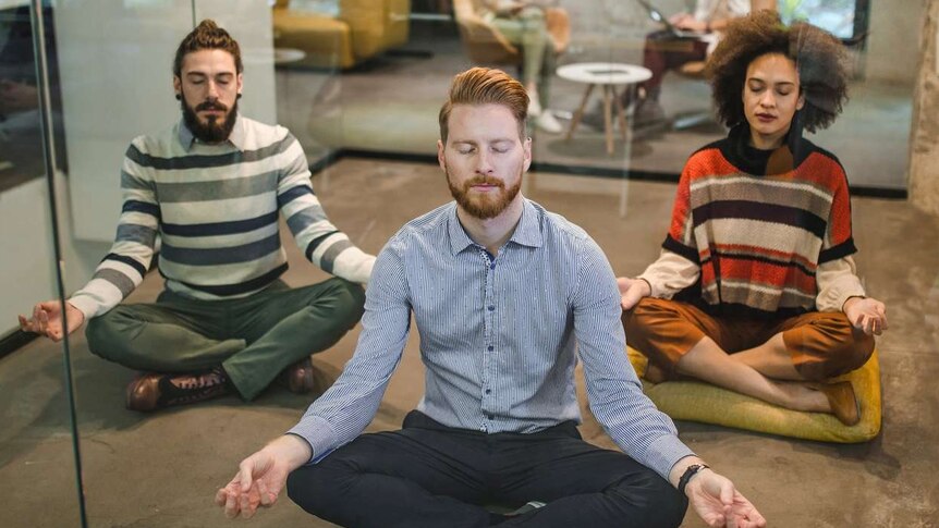 Three young workers meditate in a modern office space