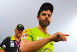 Callum Ferguson points as he holds a water bottle and trudges off as flood lights illuminate the smoke haze at Manuka Oval