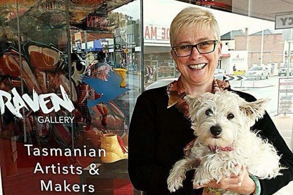 A woman holding a fluffy dog outside a gallery in New Norfolk