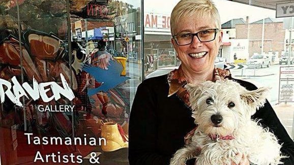 A woman holding a fluffy dog outside a gallery in New Norfolk