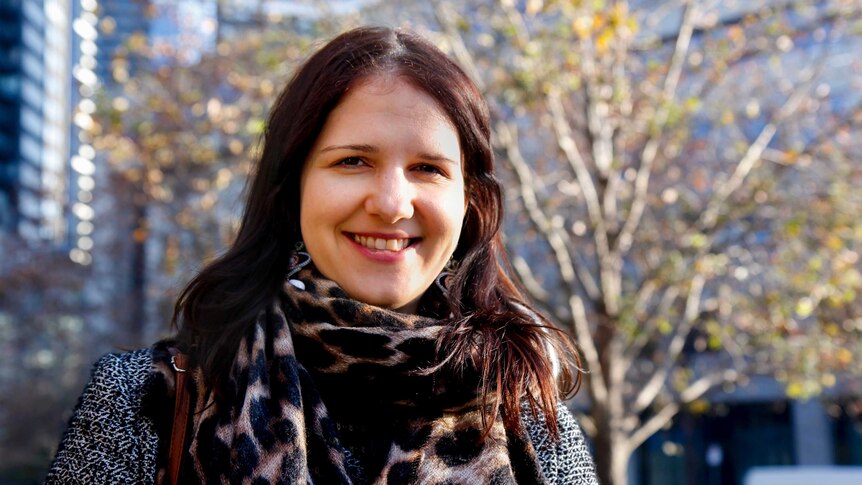 Tanja, sunlit, smiles at the camera with the Melbourne CBD behind her.