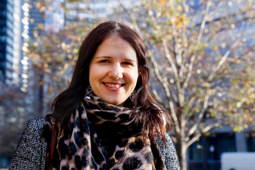 Tanja, sunlit, smiles at the camera with the Melbourne CBD behind her.