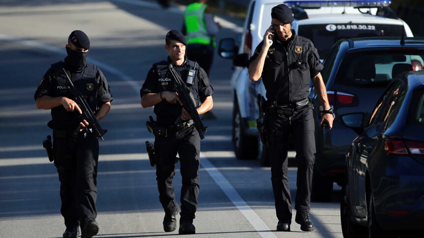 Three armed policemen walk on a road during an operation.
