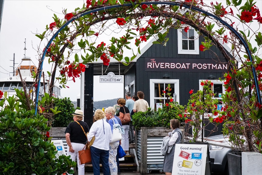 People lined up near a quaint building with a sign "Riverboat Postman".
