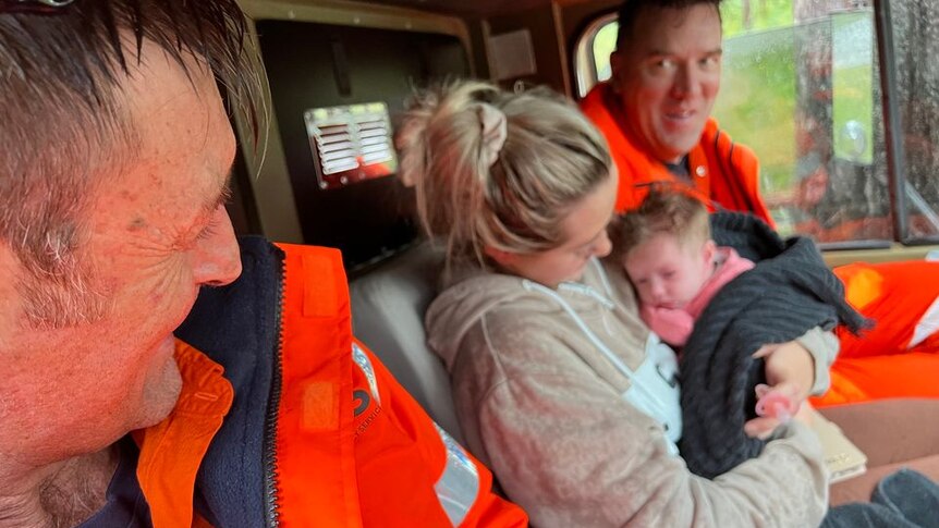 Two SES volunteers sit smiling, in a truck, with a woman and her res cued baby.