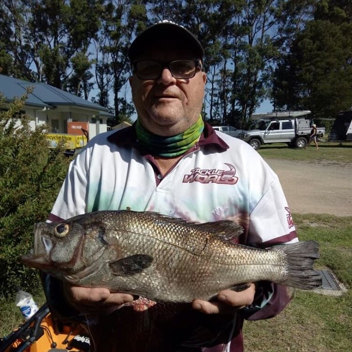 An older man with glasses holding a large fish. His face is obscured in shadow because he's wearing a cap.