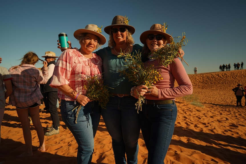 Three women standing with flowers on sand dune