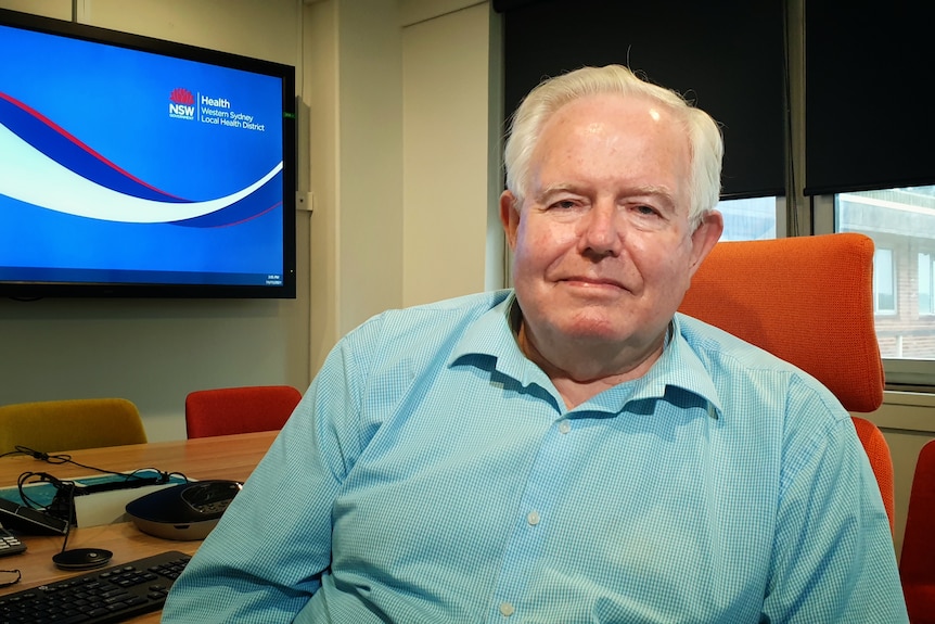 Professor Glen Maberly pictured wearing a green shirt in an office near a computer screen.