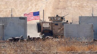 A US flagged armoured vehicle rolling through a desert location