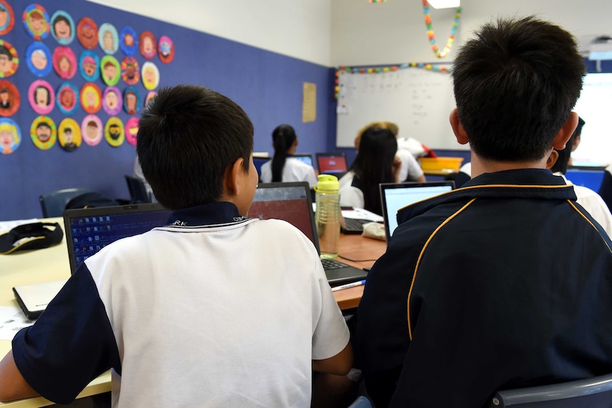 Children sitting at a desk in a classroom photographed from behind.