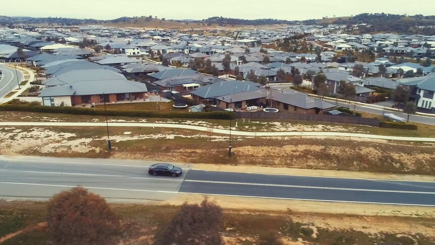 An aerial photo of a car driving along a road next to a newly developed suburb.